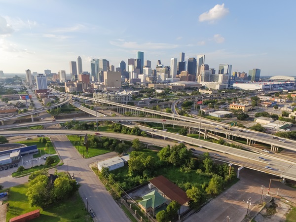 Aerial view of Houston, Texas, showcasing the city's extensive highway system and downtown skyline in the background on a clear day.