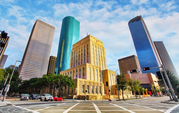 Downtown Houston skyline featuring tall modern skyscrapers with a historic courthouse in the foreground, and a wide intersection with crosswalks in front.