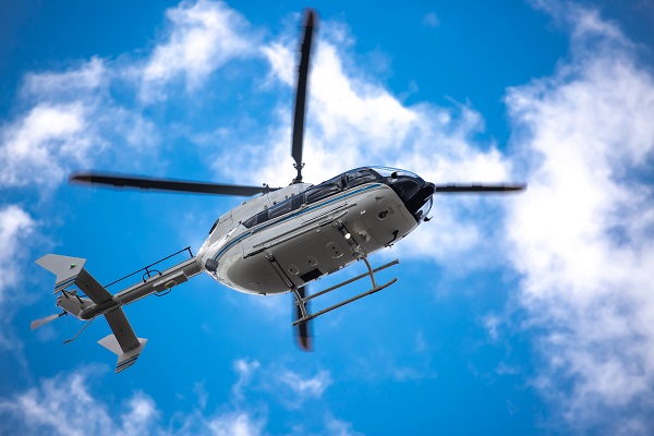 Helicopter flying against a blue sky with clouds, captured from a low angle.